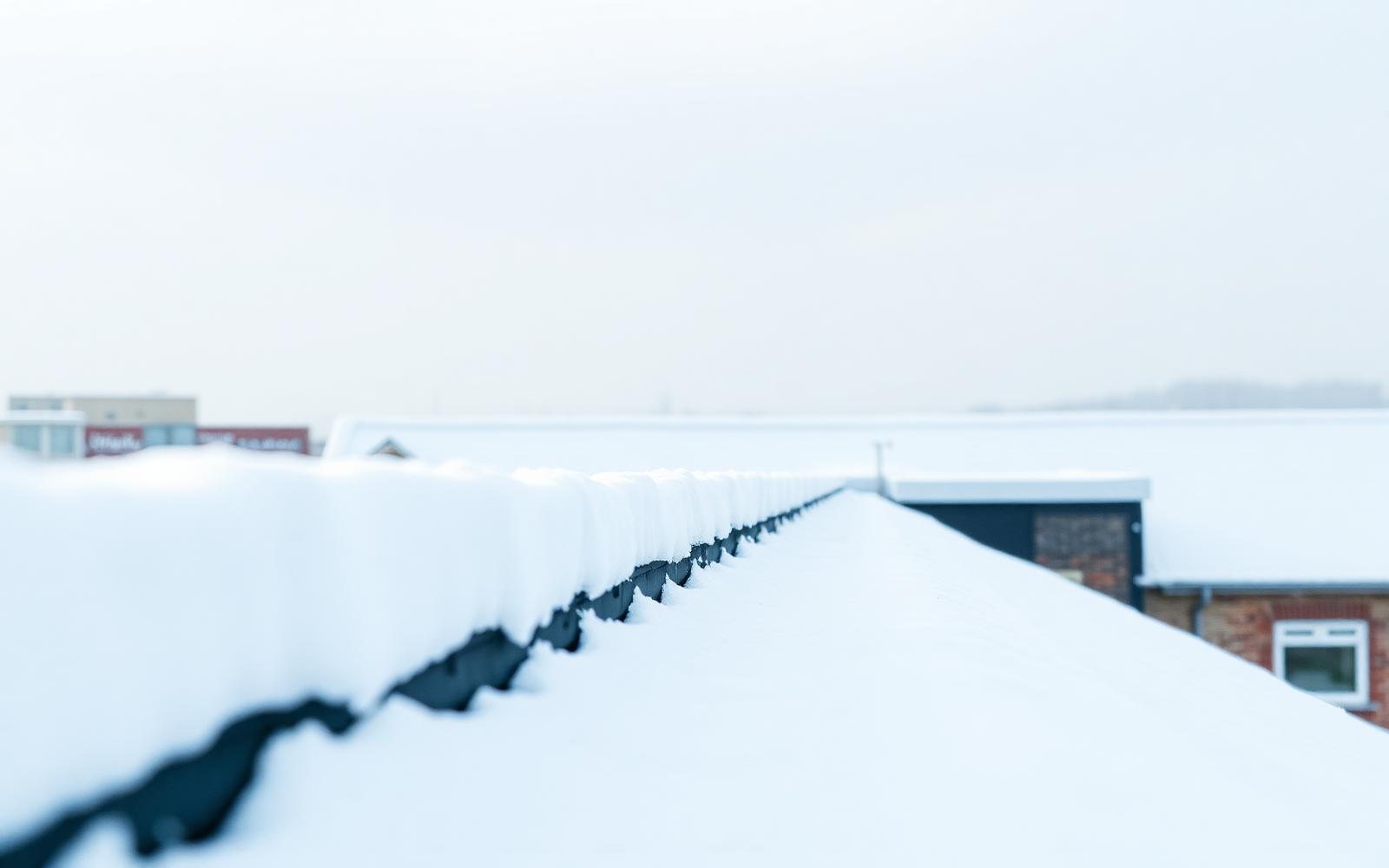 Närbild på ett stort platt industritak täckt av tjock snö med snödrivor längs takkanten
