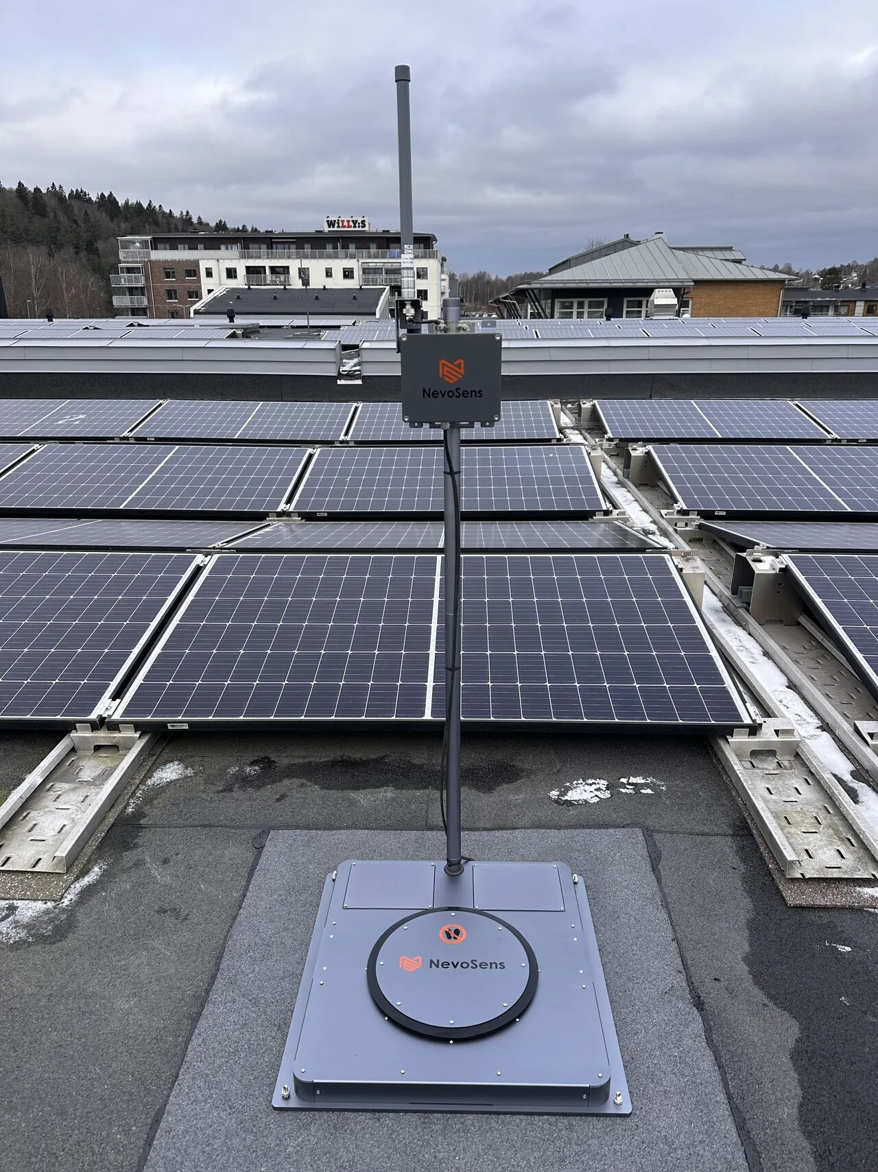 Close-up of a NevoSens snow sensor mounted on a roof next to solar panels at an ICA property in Gothenburg
